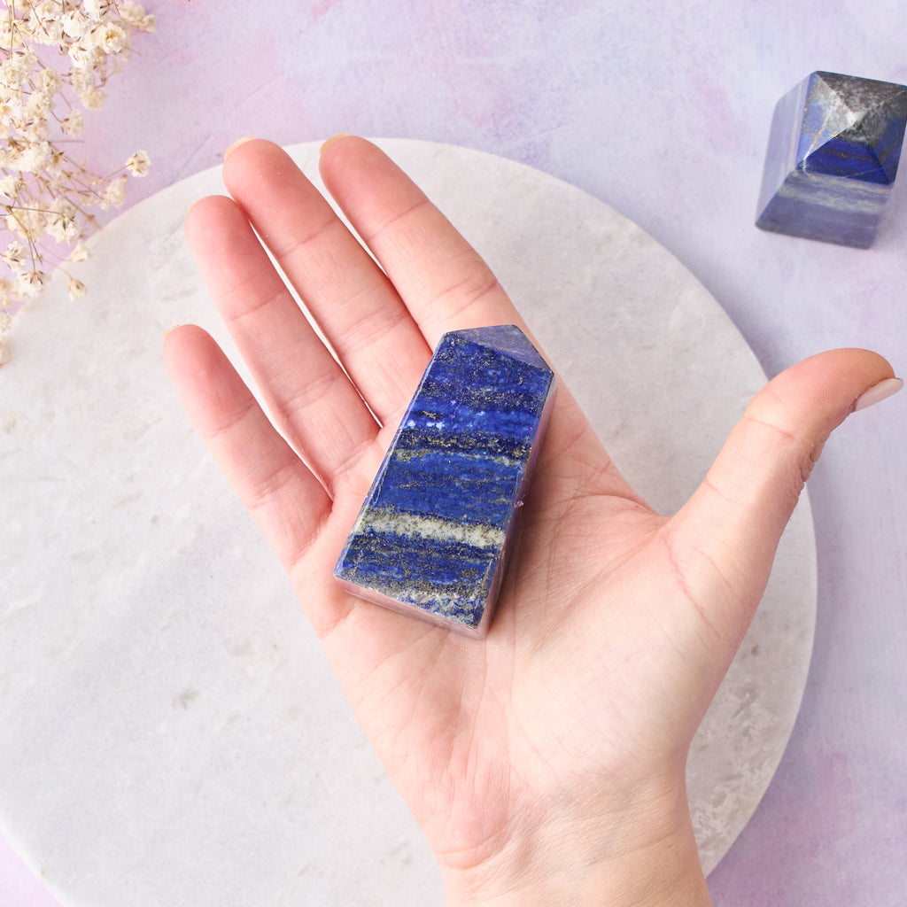 Ett lapis lazuli-torn som hålls i en hand, mot en vit bakgrund med rosa-lila toner.