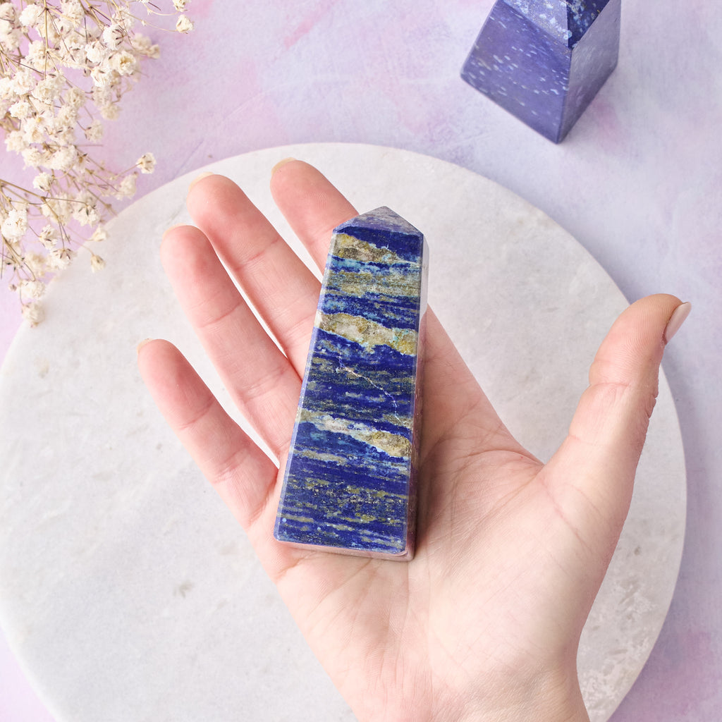 Ett stort lapis lazuli-torn som hålls i en hand, mot en vit bakgrund med rosa-lila toner.