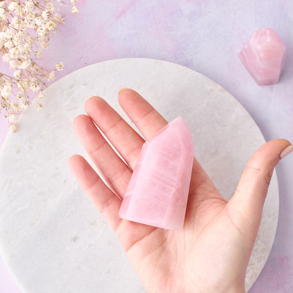Ett mindre rosenkvartstorn sett uppifrån, hålls i en hand, mot en vit bakgrund med rosa-lila toner.