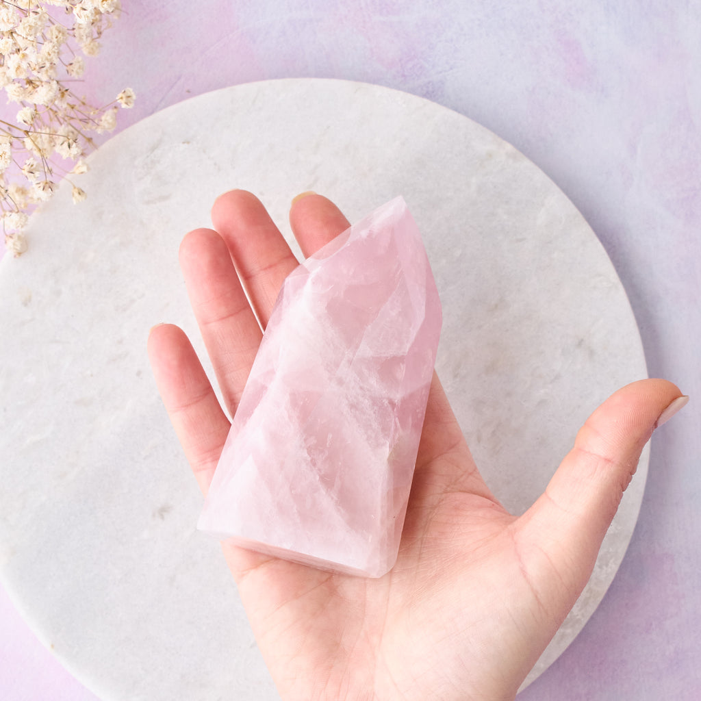 Ett rosenkvartstorn sett uppifrån, hålls i en hand mot en vit bakgrund med rosa-lila toner.