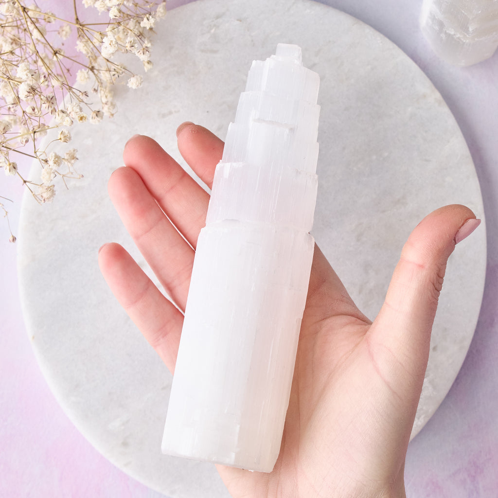 Ett stort selenittorn sett uppifrån medan det hålls i en hand, mot en vit bakgrund med rosa-lila toner.